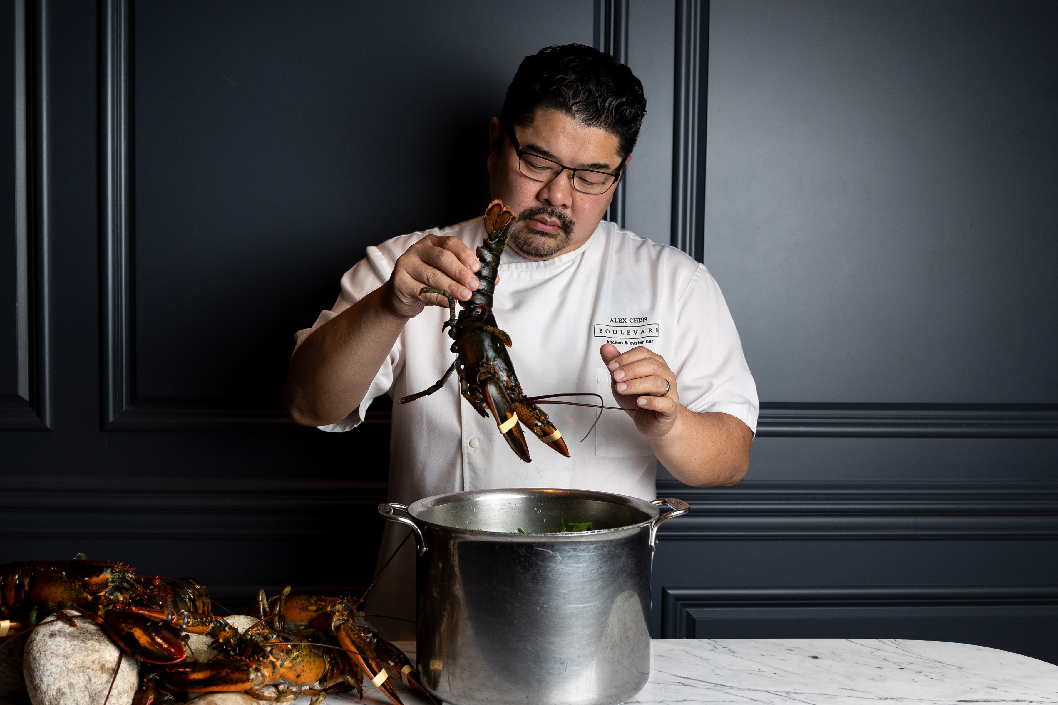 Chef Alex Chen lowering a live lobster into a stockpot at Boulevard Kitchen & Oyster Bar