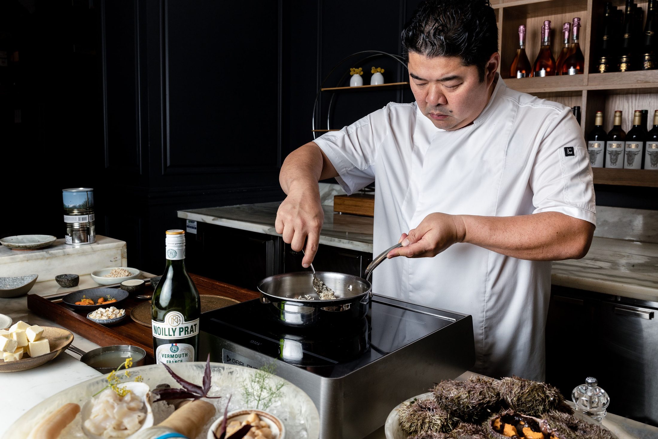 Chef Alex Chen plating a dish in a dark, wine-lined kitchen