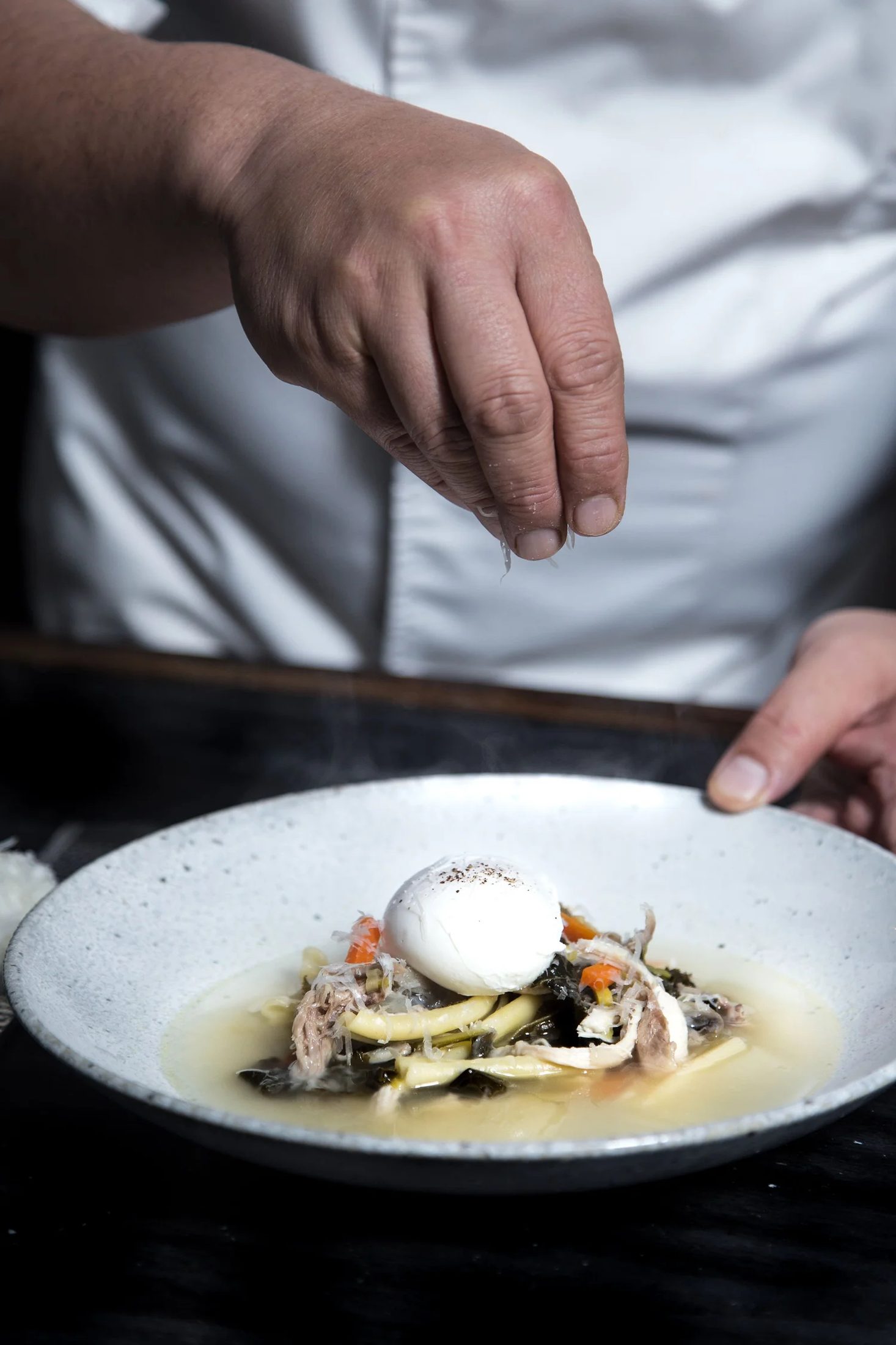 Chef Alex Chen garnishing chicken noodle soup with a poached egg