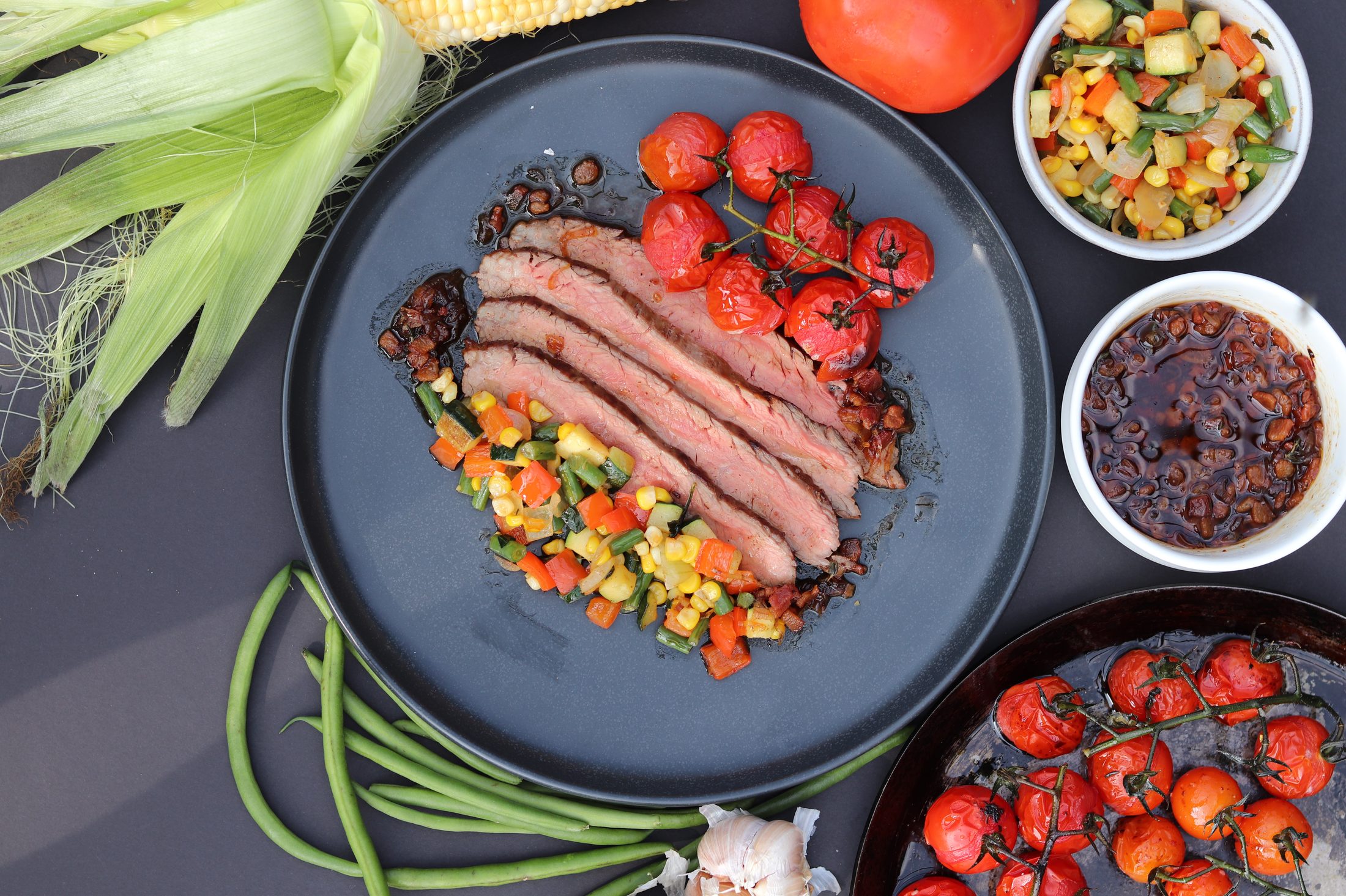 Sliced marinated flank steak with roasted vine tomatoes and corn salsa