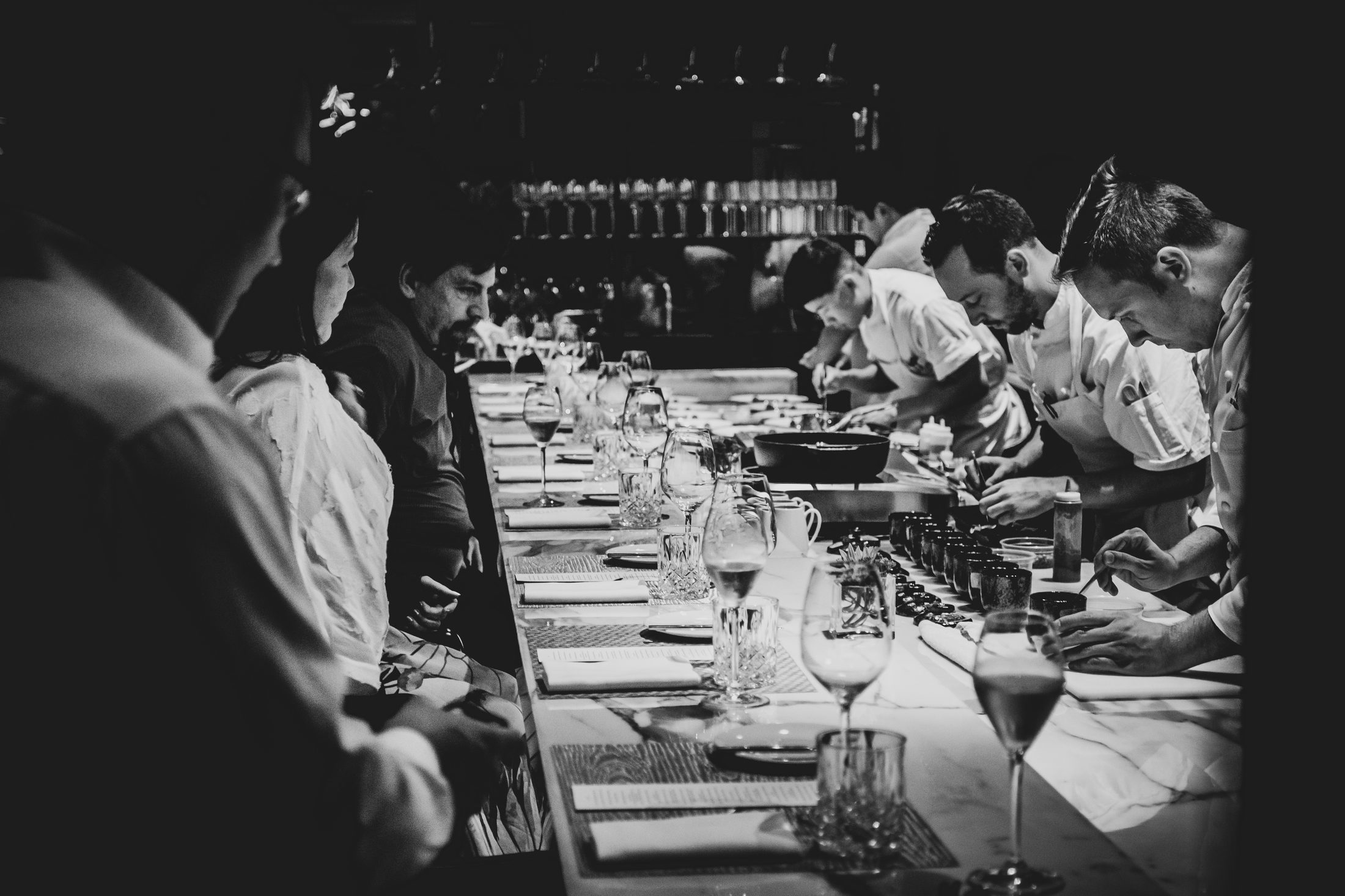 Guests seated at the marble counter watching chefs plate a TableOne dinner